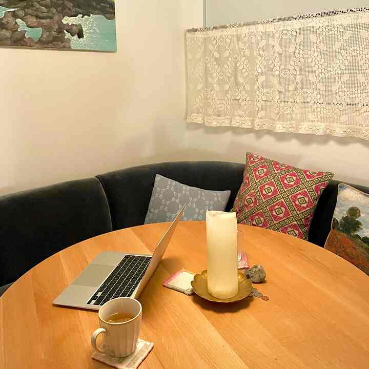 Wood tone round dining table with black L-shaped sofa featuring assorted cushions in a cozy dining room