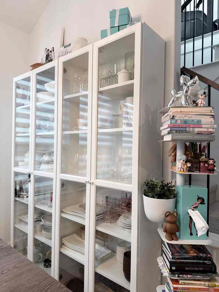 White-toned dining room featuring neatly organized glass-door storage cabinets and shelves with books and decorative items creating cozy atmosphere
