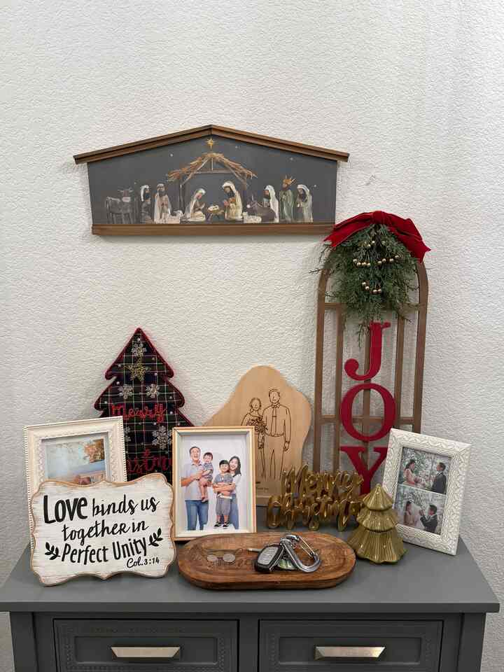 Cozy space featuring white textured wall and gray cabinet topped with Christmas-themed objects and family photo frames