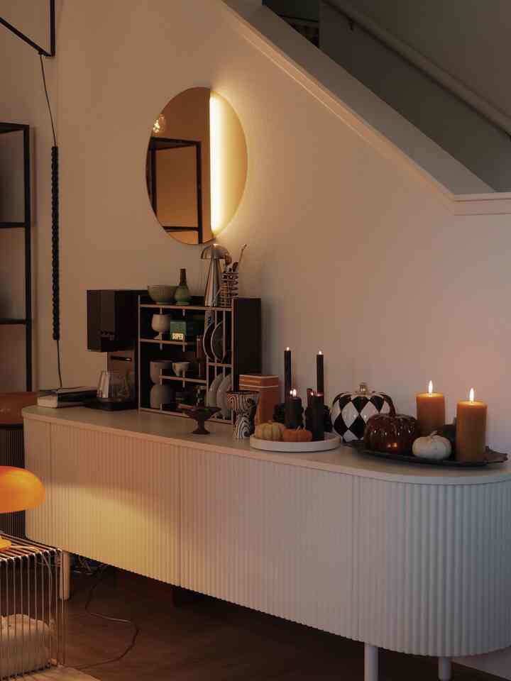 Orange and black toned living room featuring a white sideboard adorned with various Halloween candles and objets, creating a cozy atmosphere