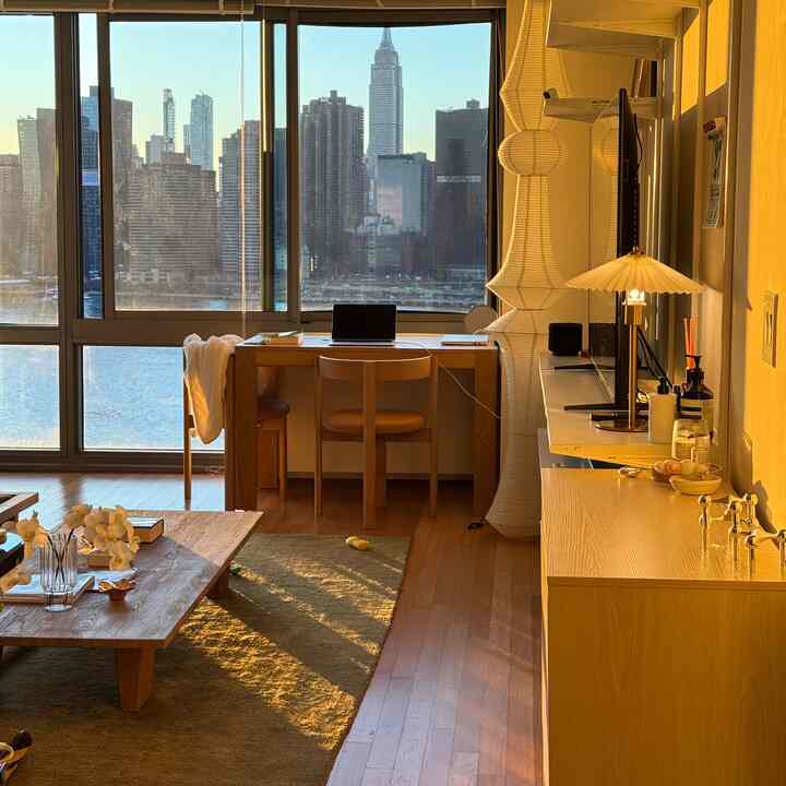 Warm wood tone living room and home office featuring natural sunlight and a city skyline view through large windows with a cozy atmosphere