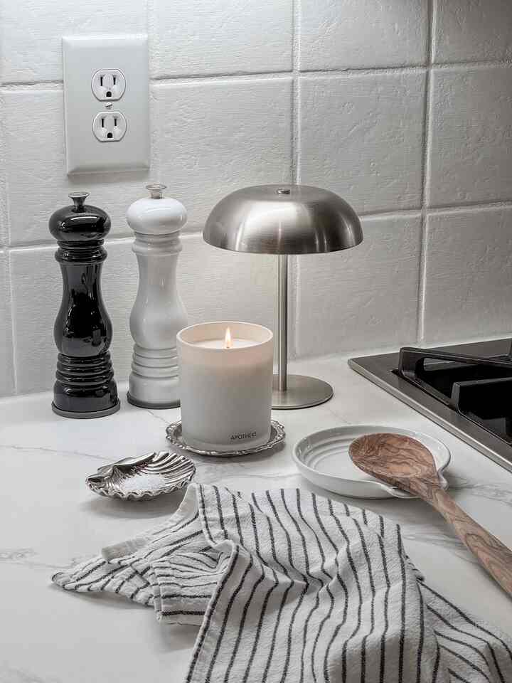 White and stainless steel kitchen counter featuring a lit candle and seasoning tools creating a calm atmosphere