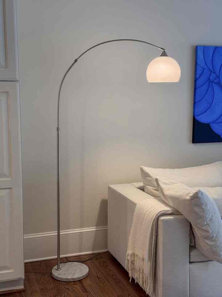 Bright white and wood-tone living room featuring a sofa and an elegant floor lamp with a cozy, clean interior atmosphere