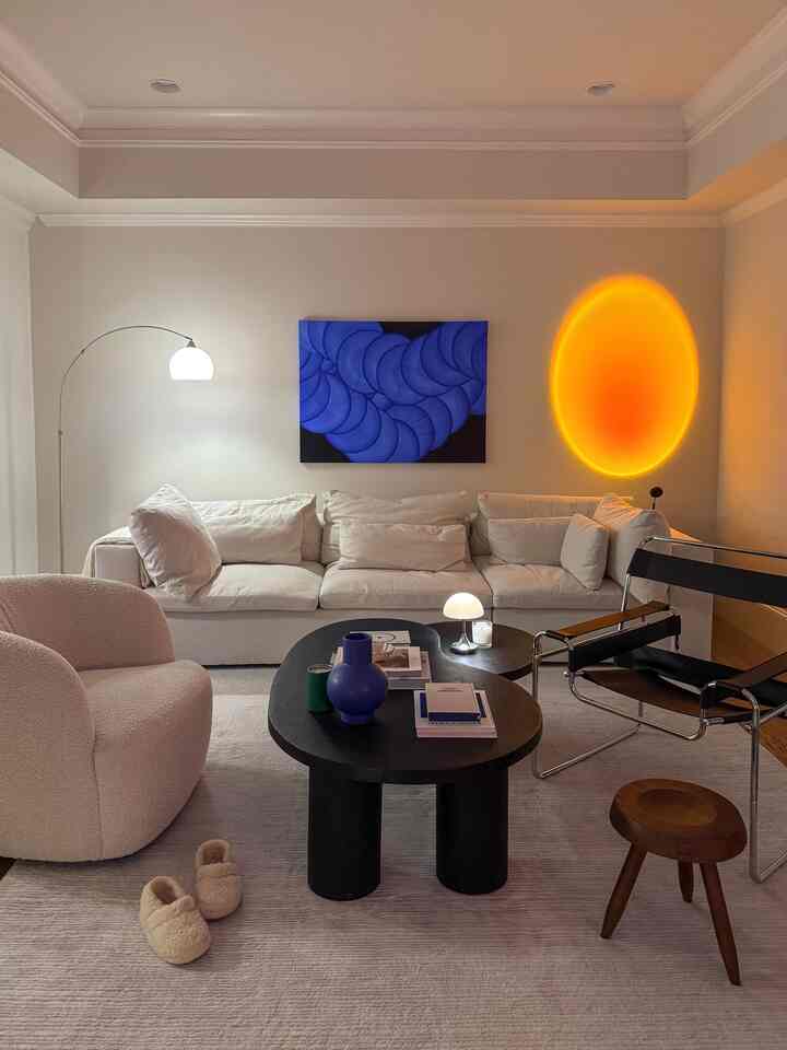 A white and wood-toned Mid-Century Modern living room featuring a sofa, armchair, stool, and floor lamp in a cozy setting