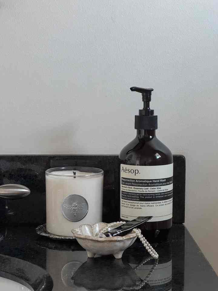White and black toned bathroom countertop featuring aromatic hand wash and candle in a clean setting