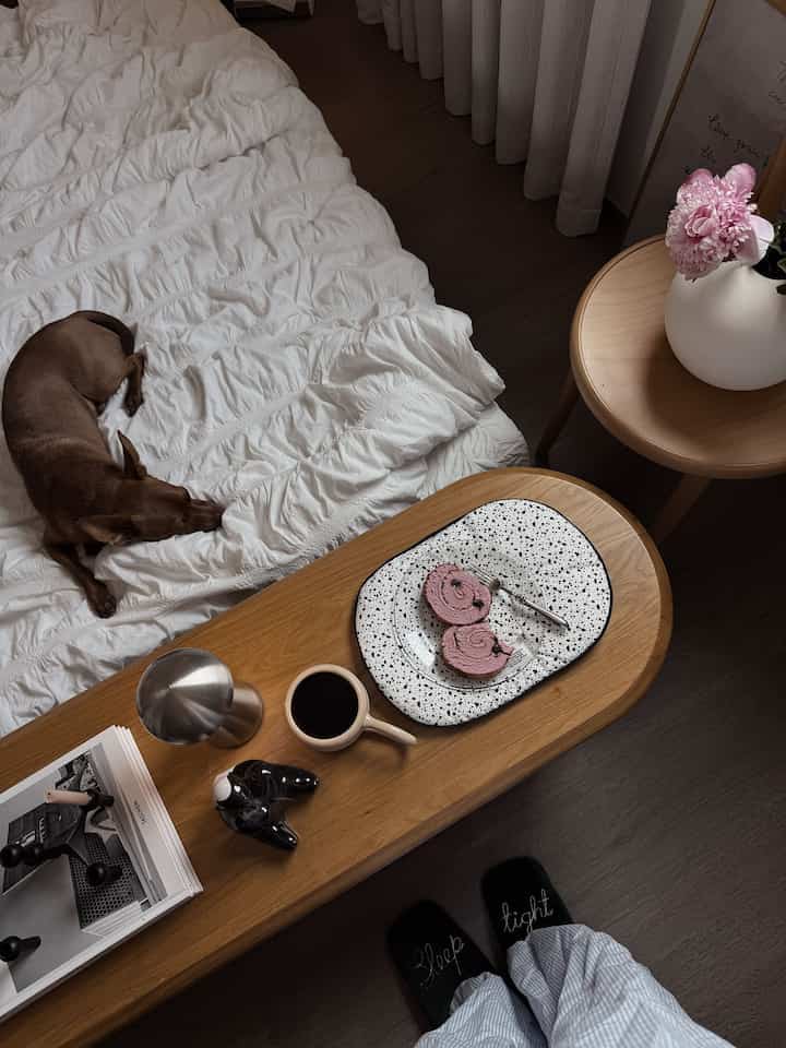 ナチュラルな木目調の寝室、白いベッドカバーと茶色の犬が配置された落ち着いた雰囲気のインテリア