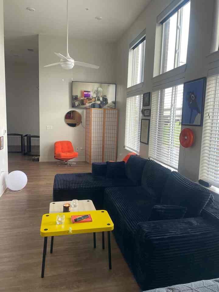 Natural toned living room featuring black sectional sofa, orange armchair, and yellow side table in a bright, tidy space