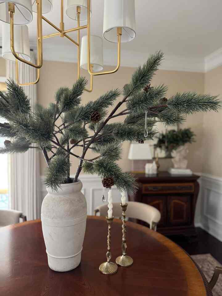 Beige-toned dining room featuring a large wooden dining table with pine branch centerpiece, gold chandelier and candles in a simple natural setting
