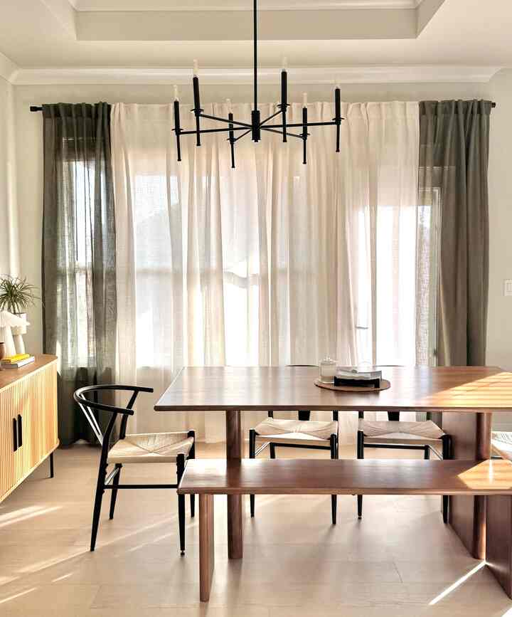 Natural modern dining room with light beige and dark olive curtains, featuring a wooden dining table and chairs, accented by a black chandelier