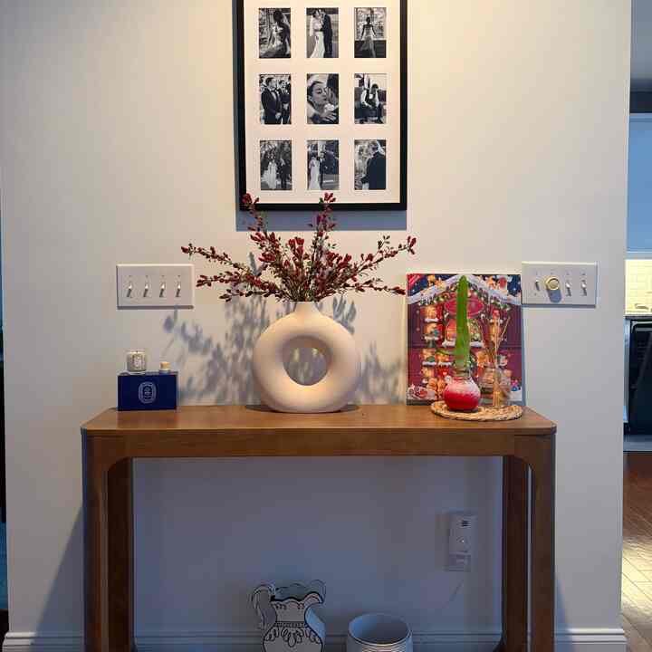 Beige and wood-toned entrance featuring a clean console table with a circular ceramic vase and photo collage on the wall