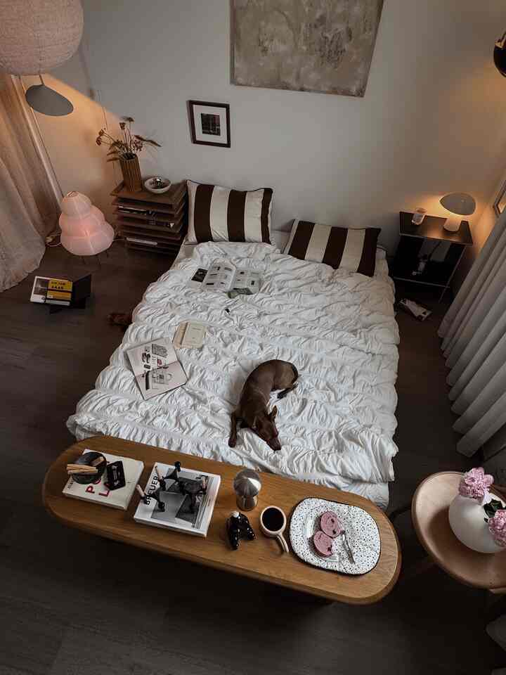 A cozy bedroom with warm brown and white tones, featuring large bedding and a dog resting on the bed