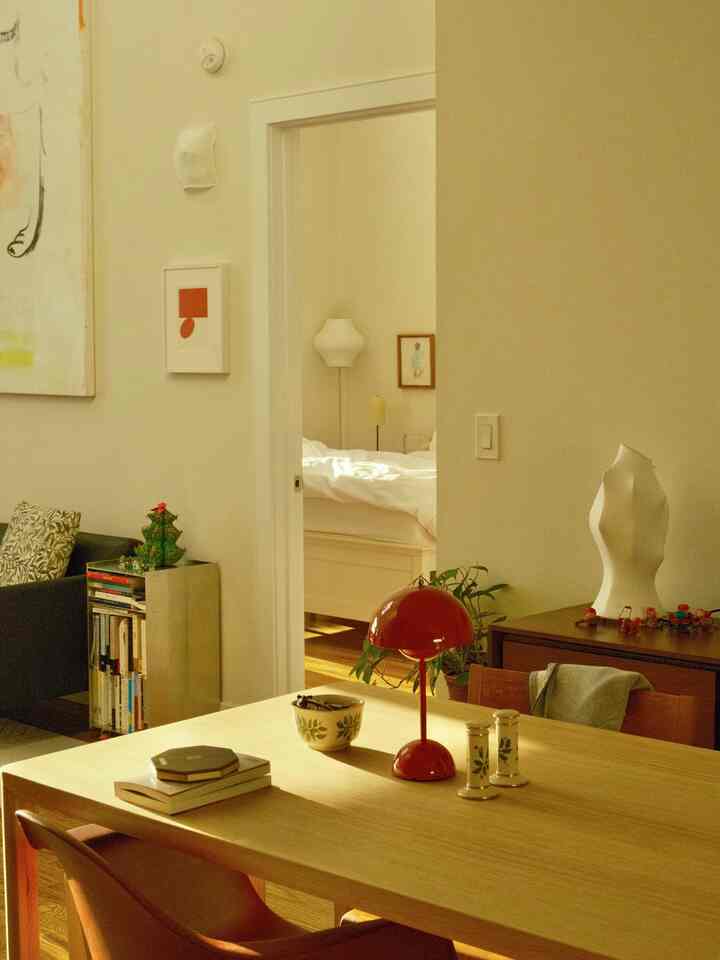 White-walled living space with wood-tone dining table, featuring a red table lamp and holiday tableware creating a cozy vibe