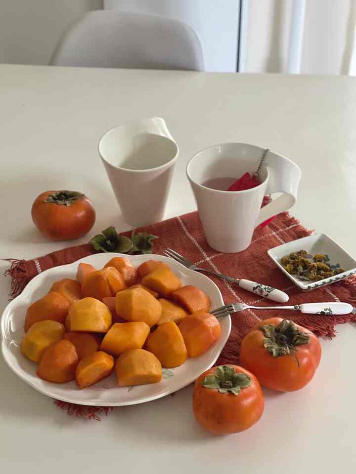 Minimal kitchen space with orange persimmons on white plate, white cups, and tea setup on white table
