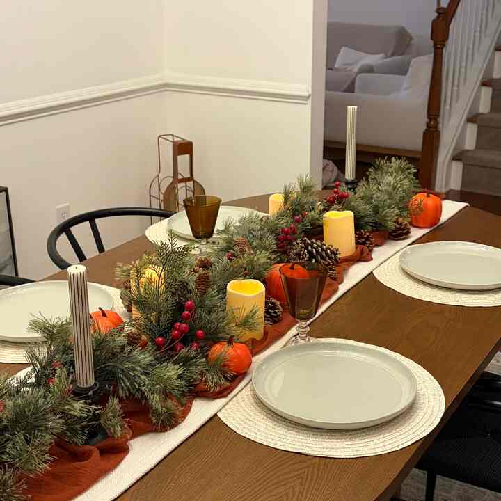 A brown and white toned dining room featuring a large wooden dining table with a runner, plates, and decorative candles creating a natural atmosphere