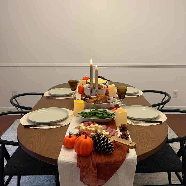 Warm wood tone dining room featuring a 4-person dining table adorned with fall table runner, candles, and pumpkin decor for a home party atmosphere