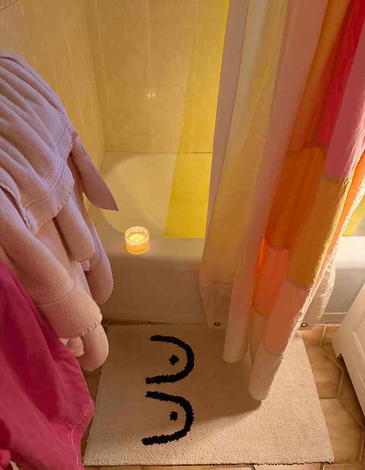 Warm-toned bathroom with pink and white towels hanging, candle on bathtub edge, shower curtain, and cream bath mat on floor