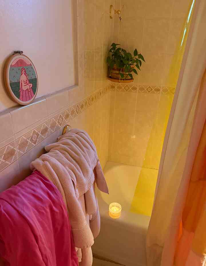 White-toned bathroom with soft pink towel and hanging plant, featuring a cozy candle-lit shower area