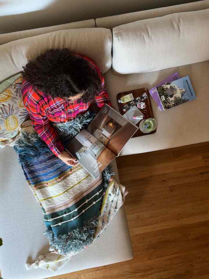 Beige sectional sofa with multicolor blanket in a living room, person seated reading a magazine creating a cozy atmosphere