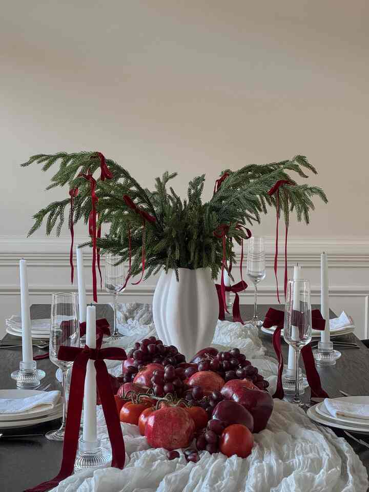 White toned dining room featuring a dining table with Christmas decorations, fruit centerpiece, and green foliage, creating a cozy home party setting