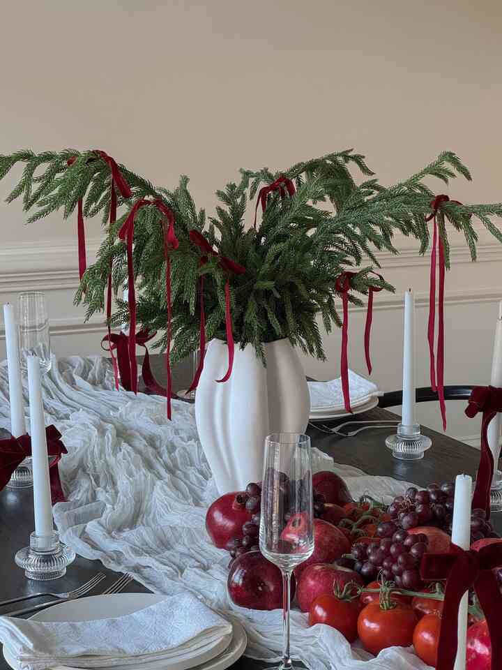 Dining room table in white and red tones featuring natural table runner, candles, and green foliage creating a warm atmosphere
