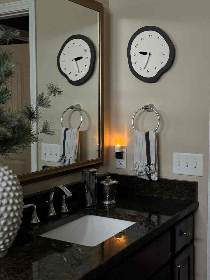 White and black toned bathroom featuring traditional wooden cabinetry, modern wall clock, towel, and a lit candle for warm ambiance