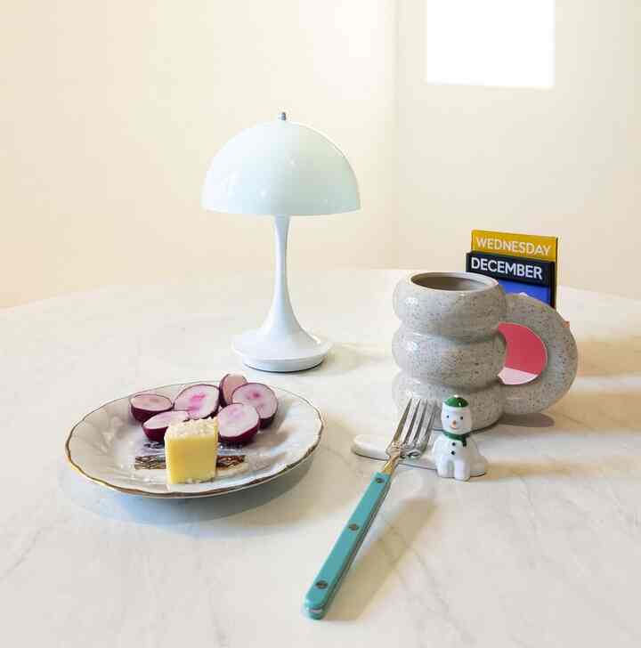White-toned minimalist table setting featuring a unique mug and table lamp in a cozy home cafe space