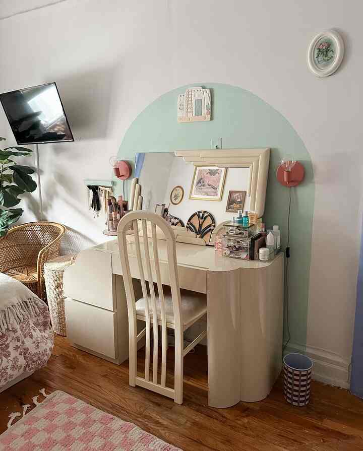 Natural toned bedroom featuring cream vanity with mirror, pink accents and wooden floor creating cozy atmosphere