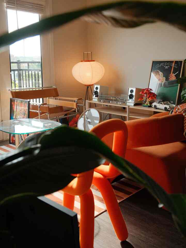 Natural-toned living room featuring orange sofa and tan armchairs, with glass coffee table and Japanese-style floor lamp