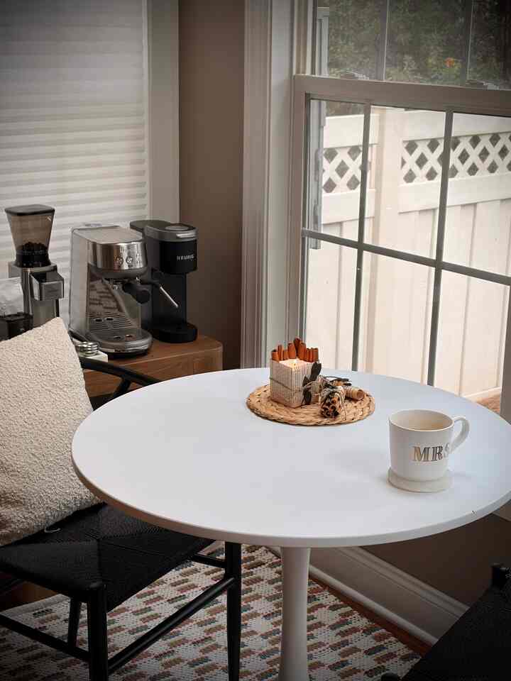 White and brown toned dining room featuring a round dining table, coffee machines, and a cinnamon candle creating a cozy minimalist home cafe nook