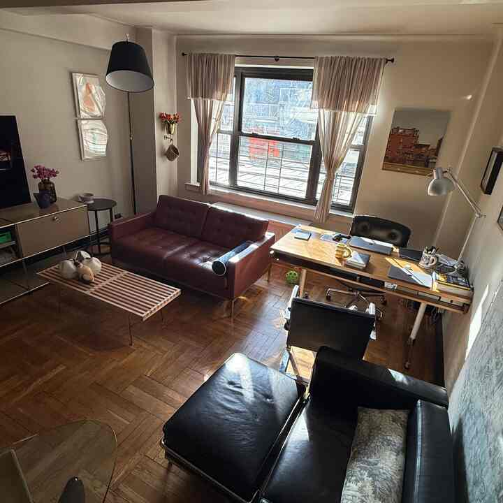 Natural wood tone flooring and dark brown, black sofas blend in a window-side home office and living room space
