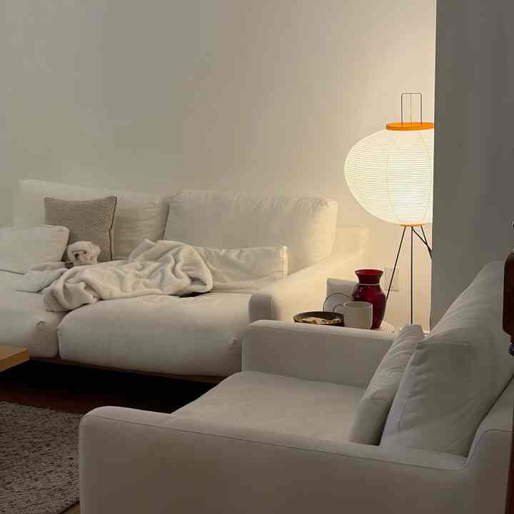 White-toned living room featuring two sofas, an armchair, and a softly lit Akari floor lamp creating a cozy ambiance