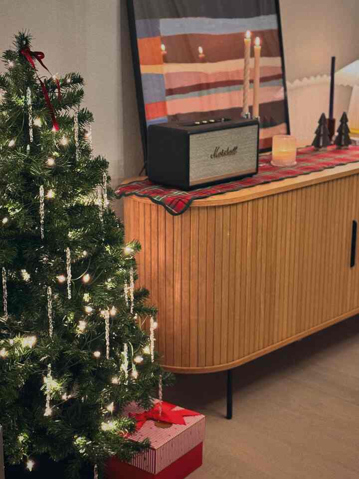 White and brown toned living room featuring a Christmas tree and decorated sideboard with soft glowing lights creating a cozy winter atmosphere