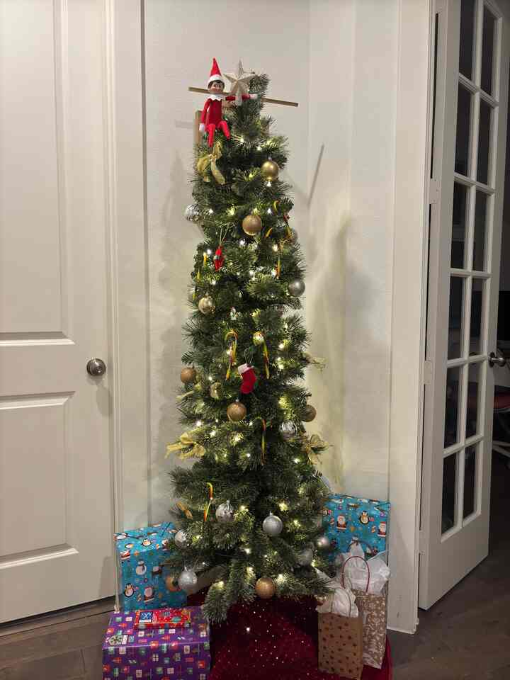 Green and gold toned pencil Christmas tree placed in cozy living room corner with festive gifts