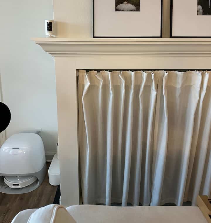 White-toned small studio living room featuring a curtained fireplace and pet supplies creating a neat, functional space