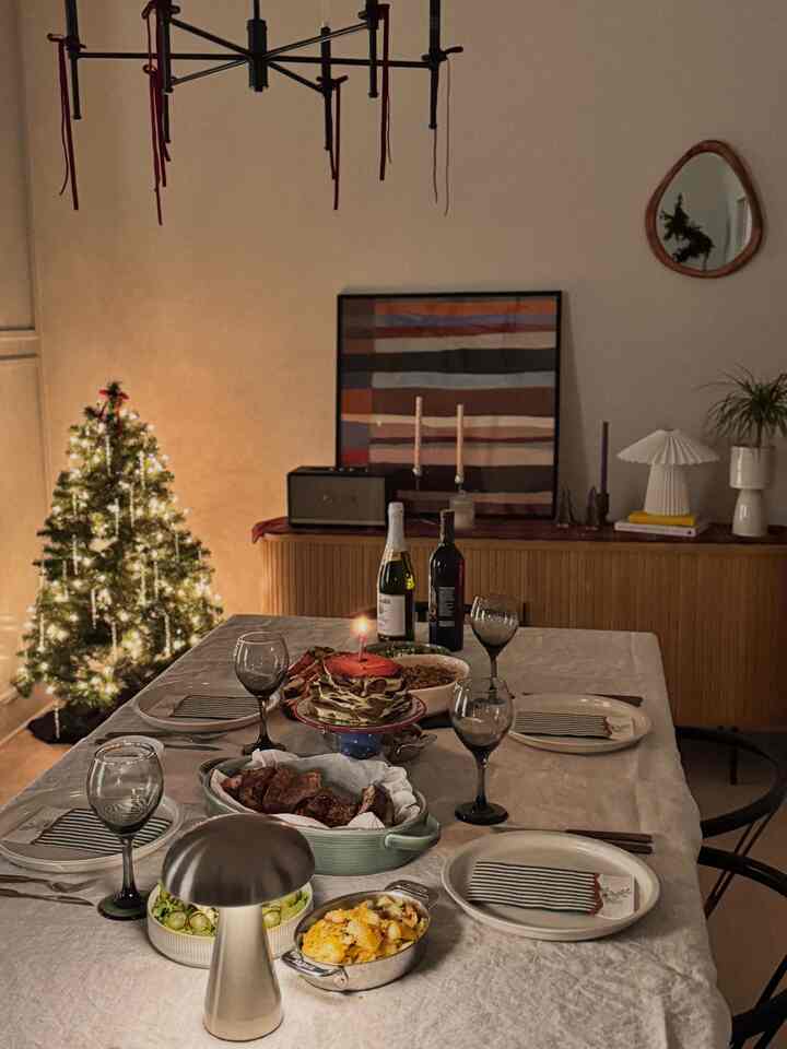 Beige and wood tone cozy dining room featuring a Christmas tree and candlelit home party dining table setup