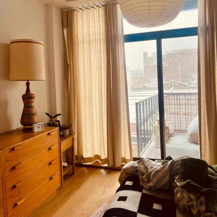 Warm beige and wood-tone bedroom featuring soft curtains, cozy bedding, and snowy view outside the sliding door