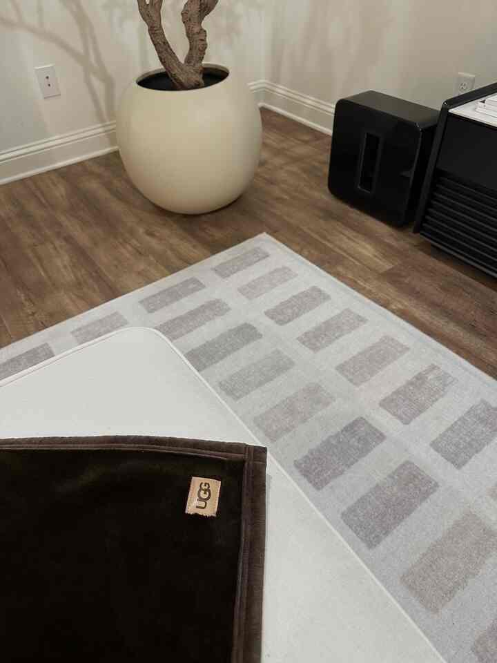 Natural light brown wood flooring with an ivory rug and a dark brown soft throw on a sofa in a living room space