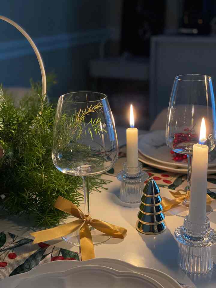 Warm gold and white toned dining table featuring lit candles, wine glasses, and a decorative table runner creating a cozy home party atmosphere