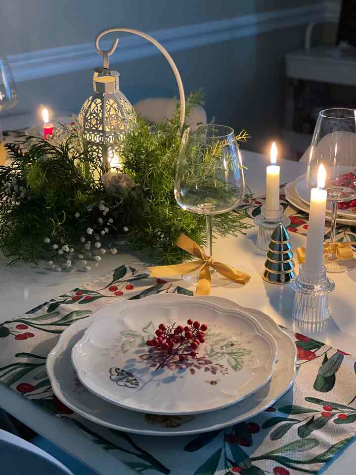 White and green toned dining space featuring a cozy Christmas home party table set with candles and wine glasses