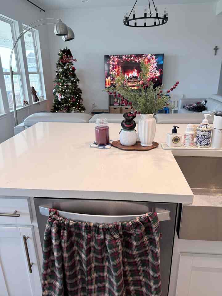 White-toned kitchen connected to living room featuring Christmas tree, countertop decor with seasonal accents creating cozy holiday atmosphere