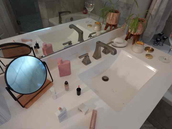 White-toned bathroom featuring a vanity with mirror, plants, and candle creating a cozy natural atmosphere