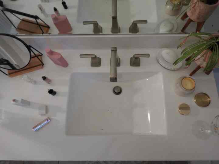 White-toned bathroom sink and mirror, vanity space featuring candles and plant on countertop