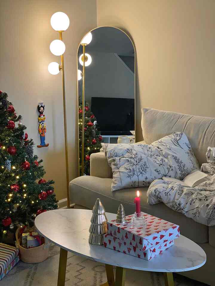 Warm beige-walled living room featuring a white sofa, Christmas tree, marble coffee table, and gold floor lamp creating a cozy relaxation space