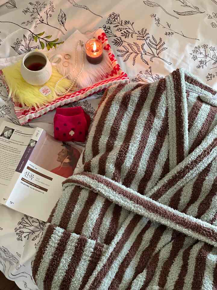 Cozy bedroom scene with a striped bathrobe, tea cup, candle, and accessories on white bedding featuring floral patterns