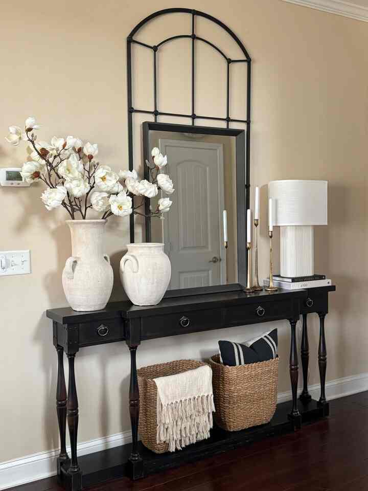 Beige-toned entrance with black console table, white magnolia flowers, and candle holders creating a natural atmosphere