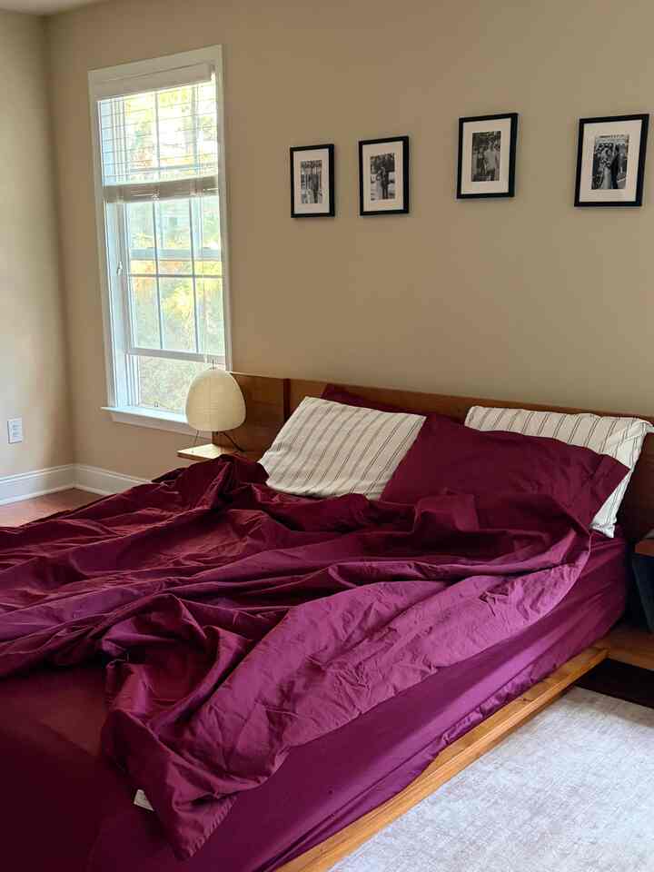 A simple bedroom with burgundy bedding on a wood tone bed frame, featuring an Akari lamp on a nightstand