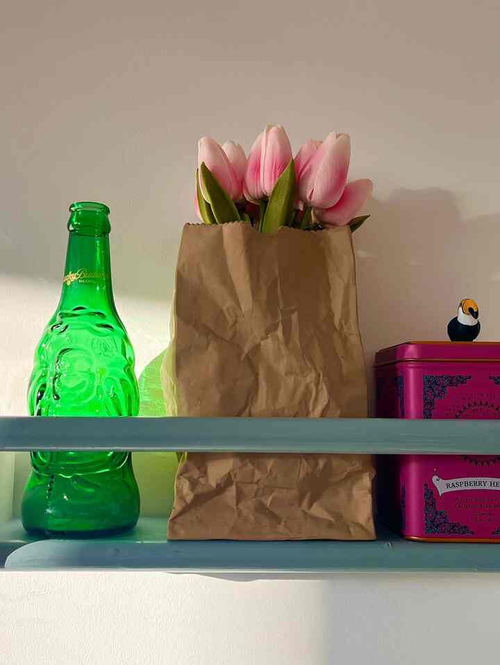 Light navy shelf featuring pink tulips in a brown paper bag, a green bottle, and a purple tin box, creating a cozy decorative vibe