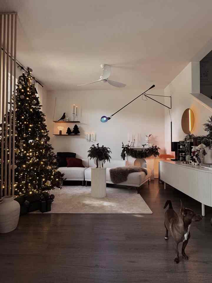 Cozy living room with warm brown wood flooring, white sectional sofa, Christmas tree, and decorative lamps creating festive ambiance