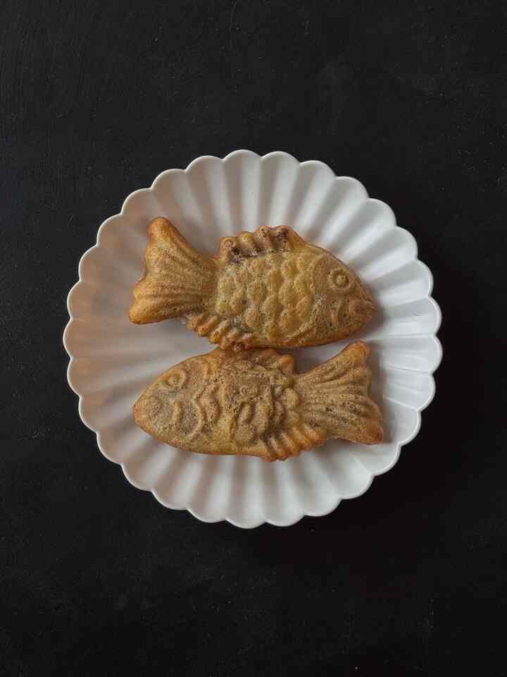 Simple dark-toned background featuring two brown fish-shaped pastries on a white scalloped plate