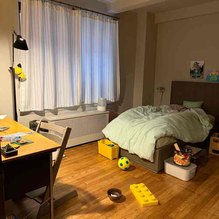Beige-toned kids' room featuring wood flooring, bed, desk, and scattered toys with storage boxes creating a cozy atmosphere